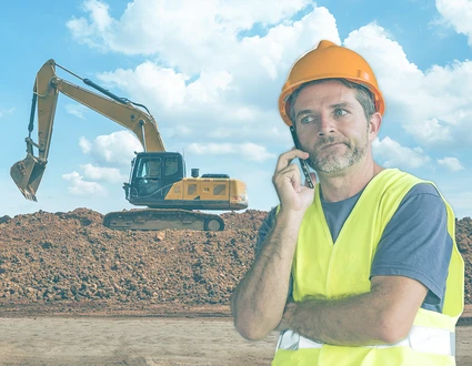 Bauleiter am Telefonieren auf einer Baustelle mit Bagger im Hintergrund