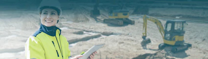 Frau mit gelber Jacke, Bauhelm und Tablet vor Baustelle mit gelben Baggern